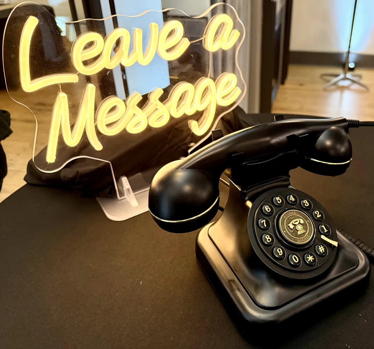 Audio guest book at a wedding reception: a vintage black rotary telephone beside a glowing Leave a Message neon sign