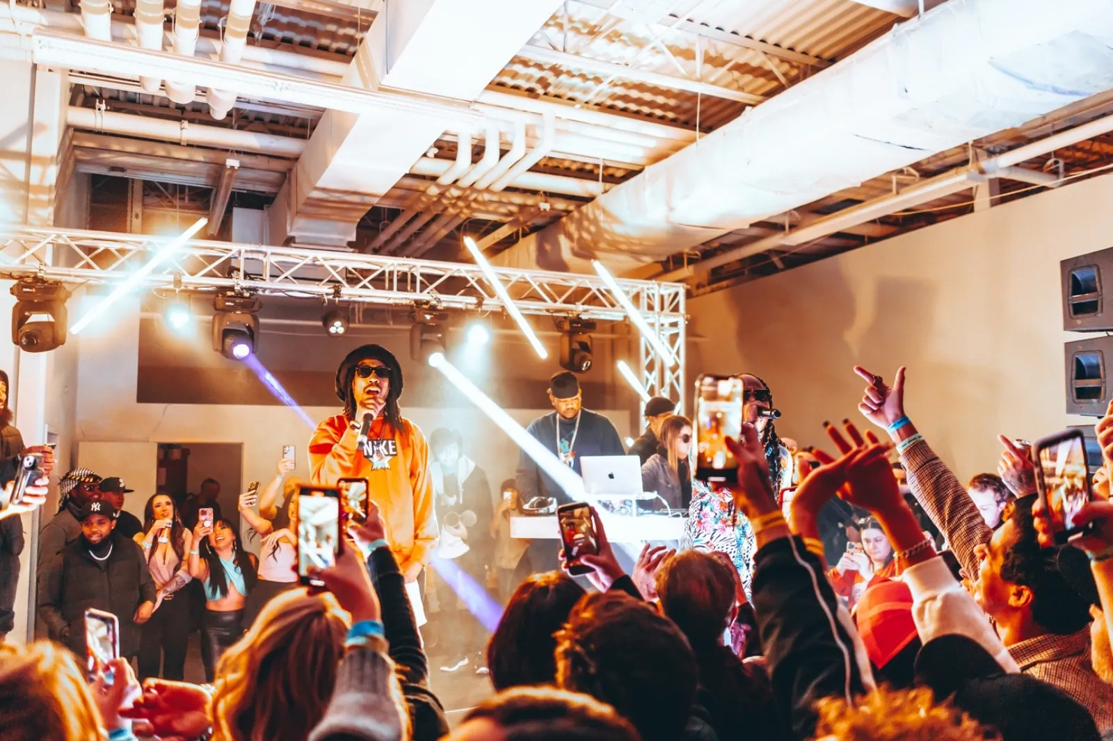Performer and crowd under truss lighting, phones in the air