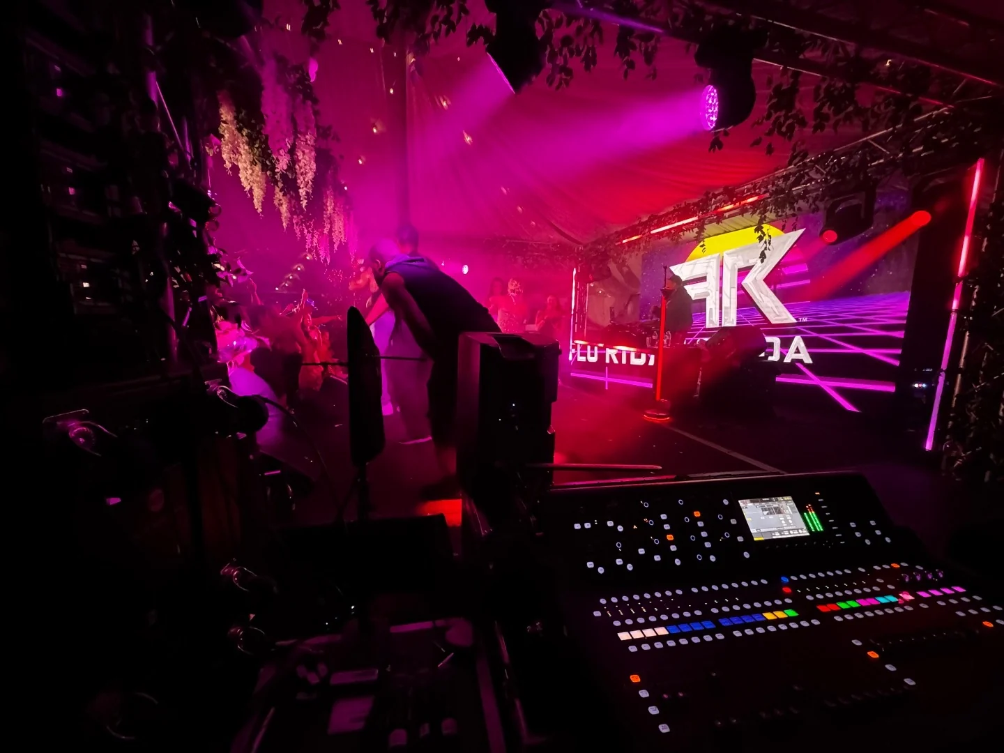 Digital mixing console at front of house, lit by the stage during a live show