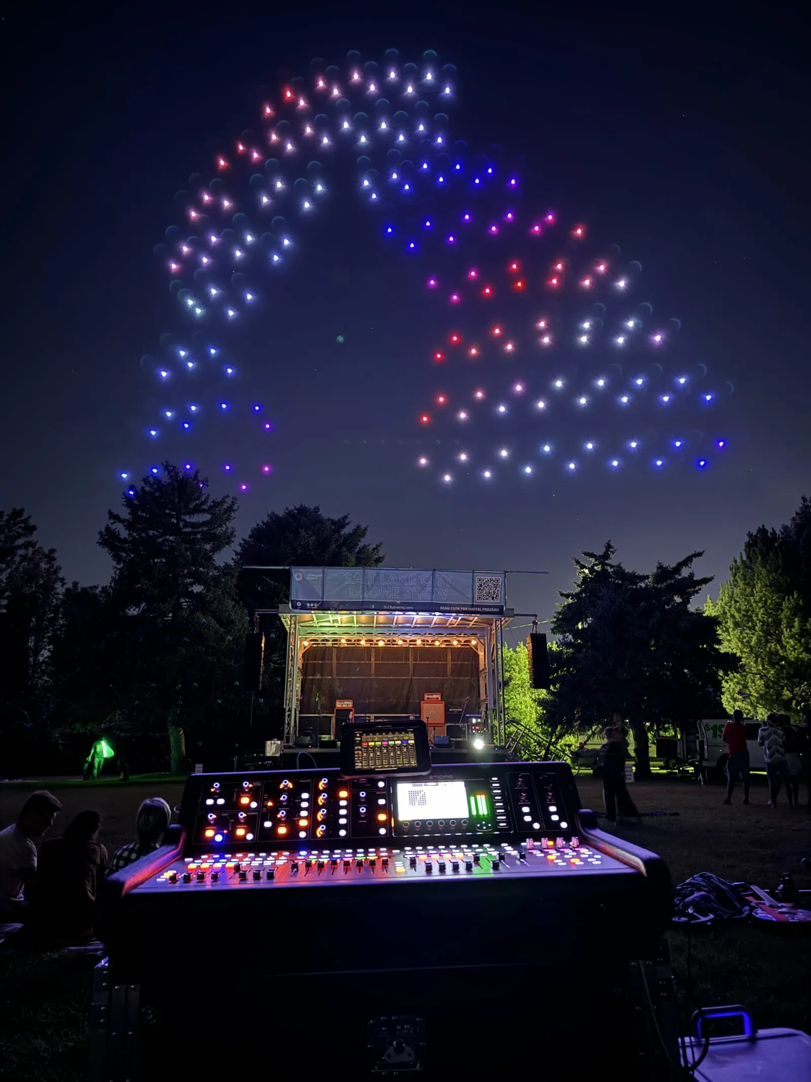 Synchronized drone light show above an outdoor evening event stage