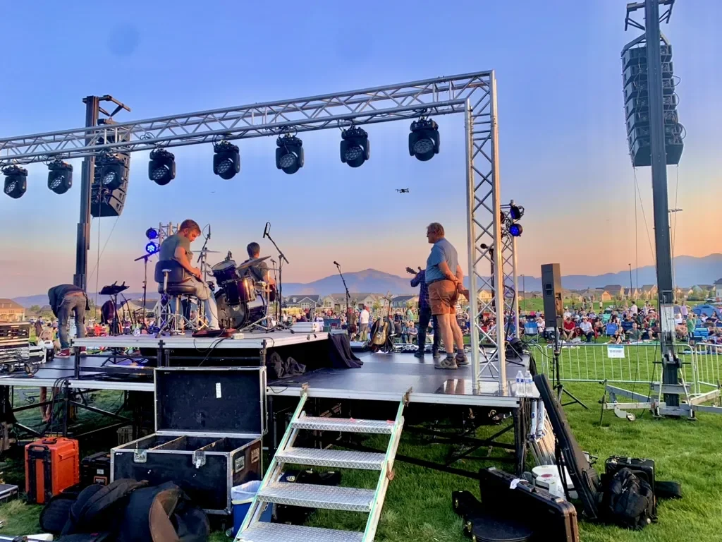 Band performing at sunset on a festival stage with the crowd on the lawn