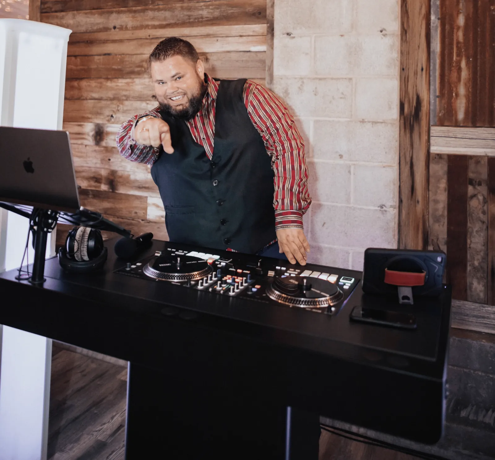 Mark Christiansen behind his DJ booth at a brick-walled wedding venue, pointing to the dance floor