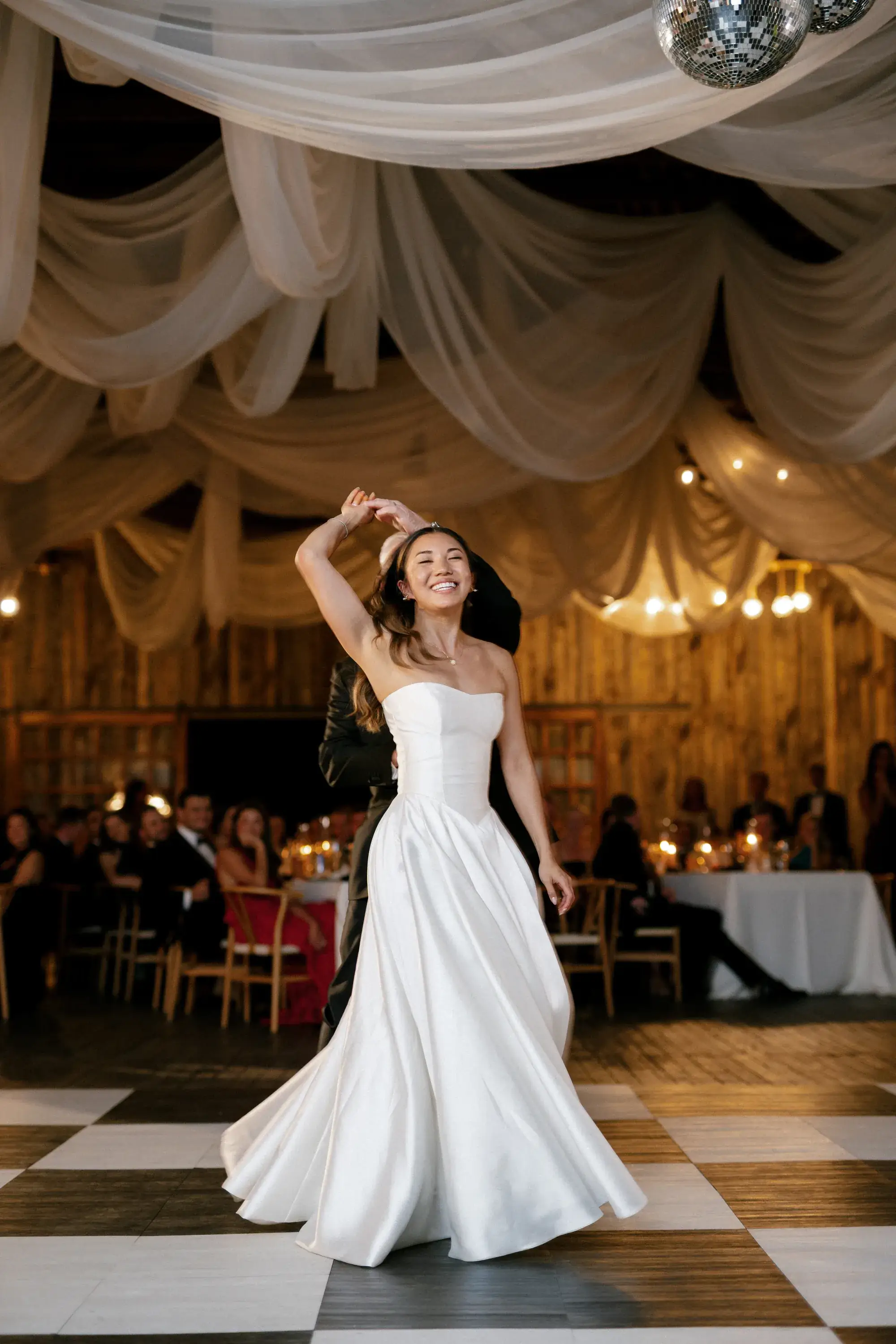 Bride spinning on a checkered dance floor beneath ivory ceiling drapes at an Idaho mountain wedding reception