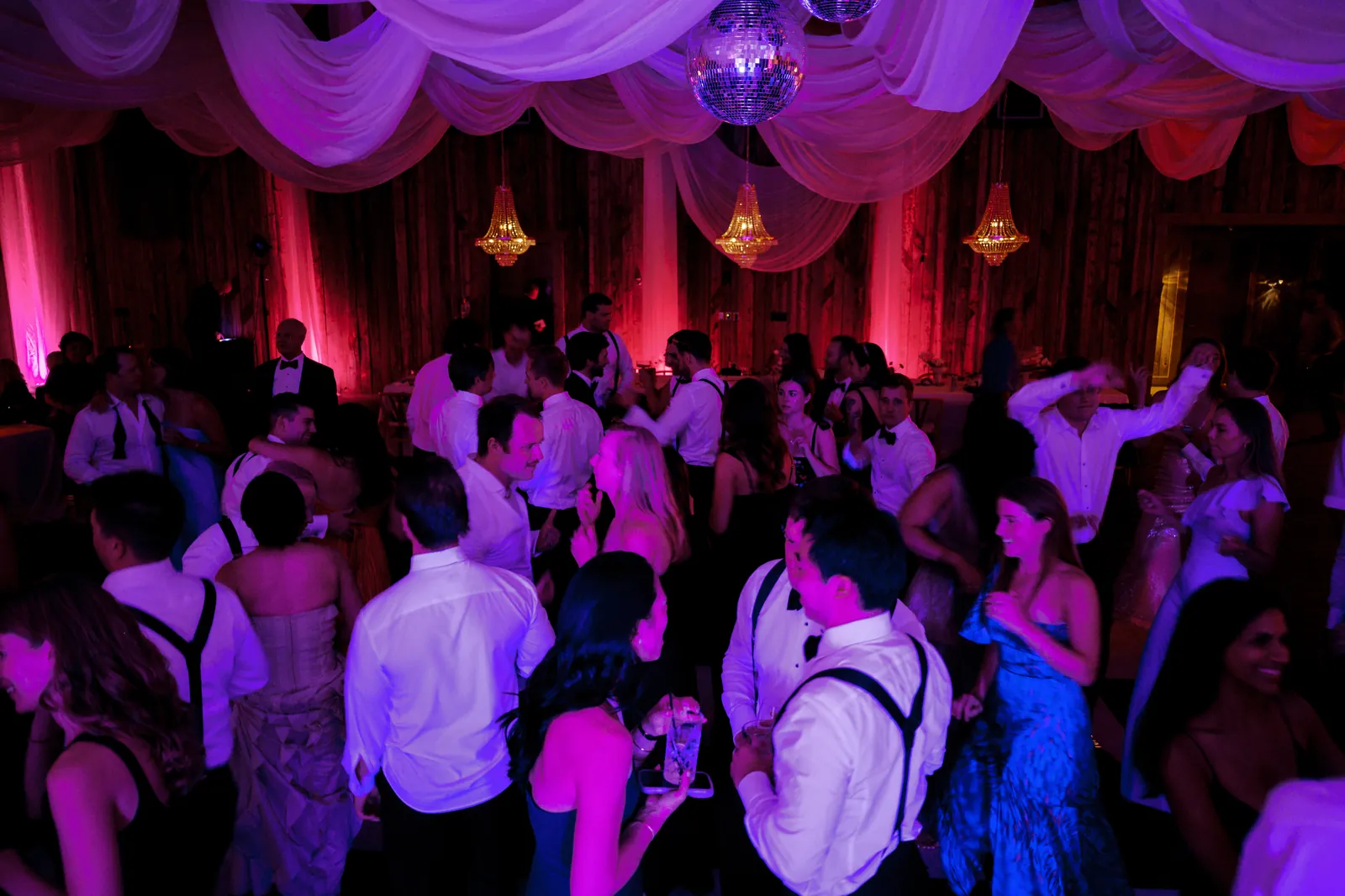 Guests dancing under a disco ball and pink lighting at a wedding reception