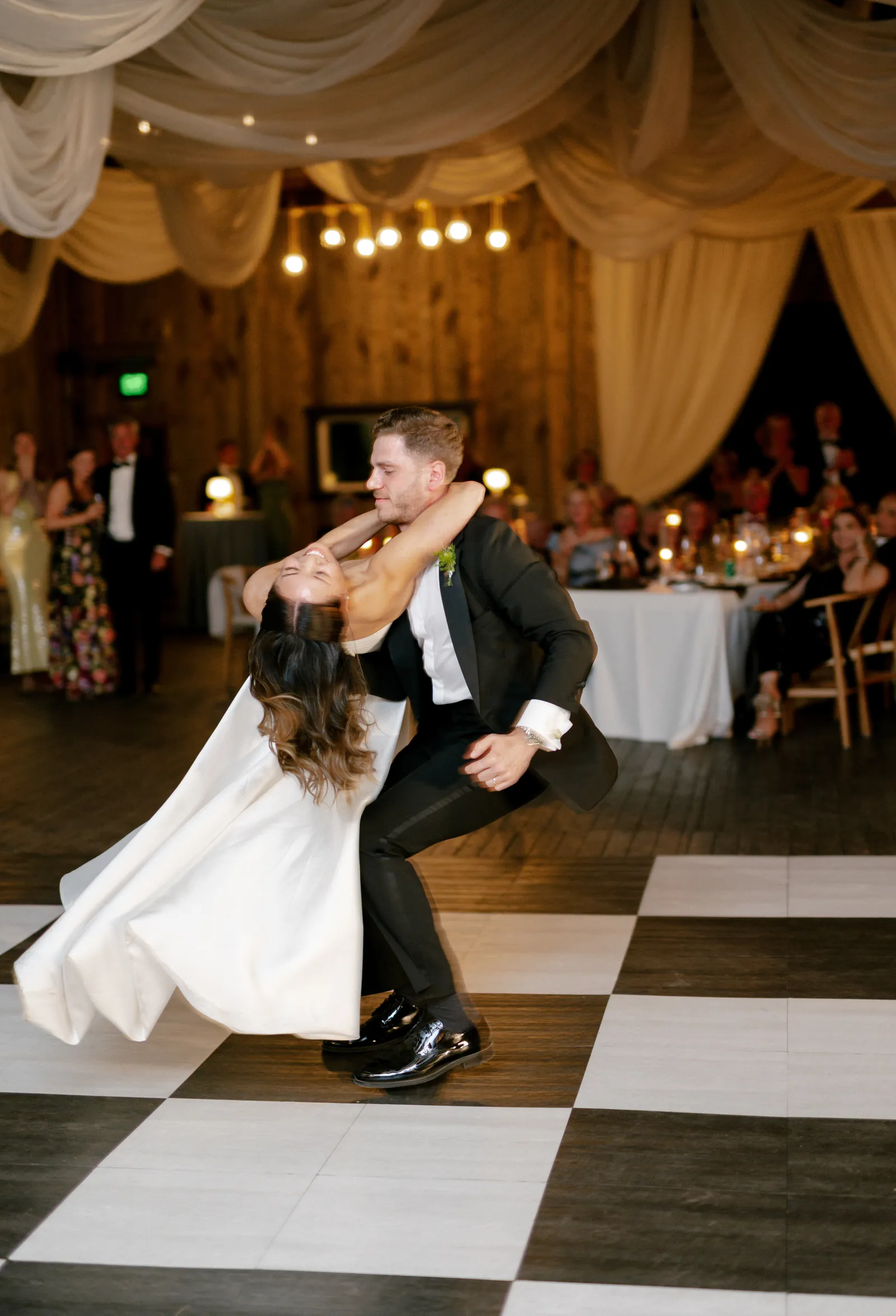 Groom dipping his bride during their first dance on a black and white checkered dance floor