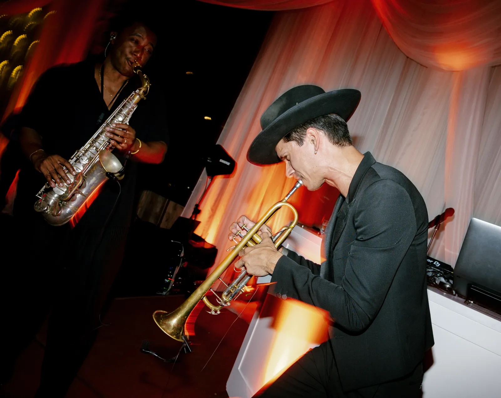 Saxophone and trumpet players performing live alongside the DJ under warm stage light