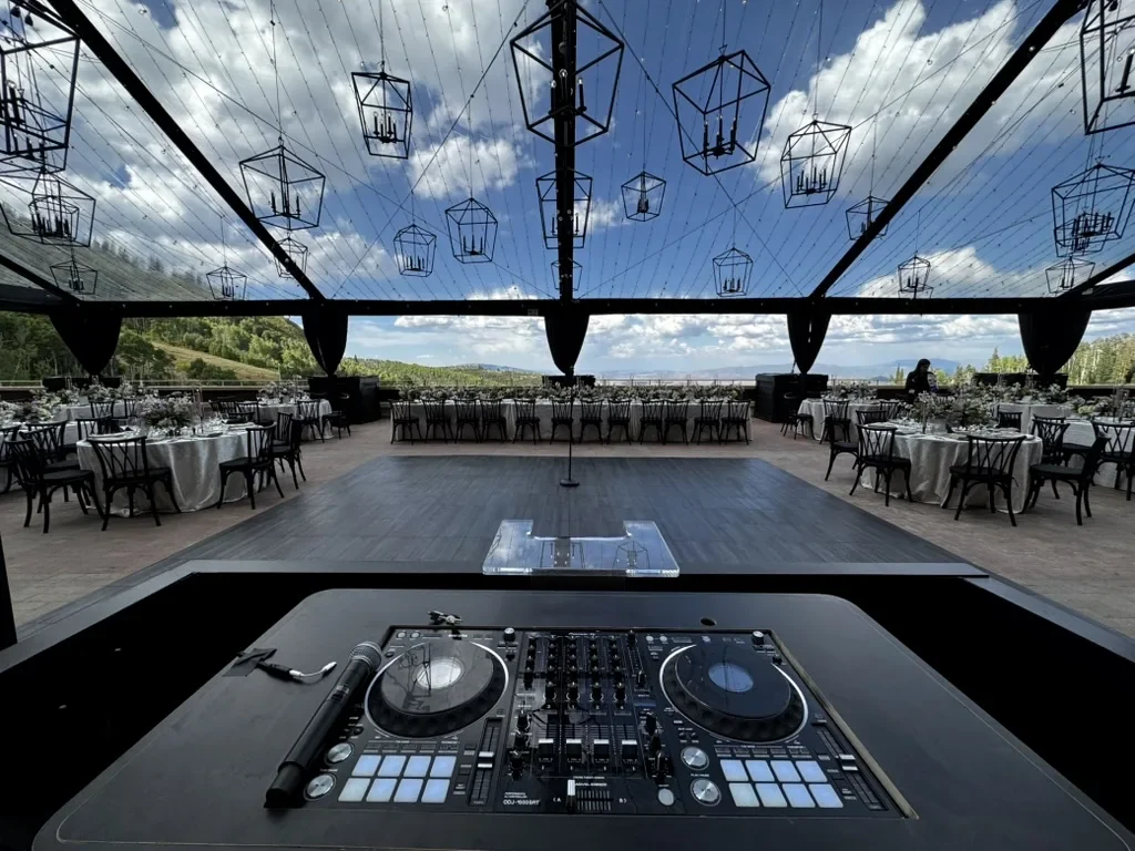 Wedding reception set and ready hours before guests arrive, a glass pavilion with hanging lanterns and the DJ decks in the foreground